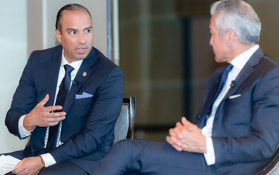 Tayde Aburto seated in a public conversation, gesturing mid-sentence while the other participant listens.